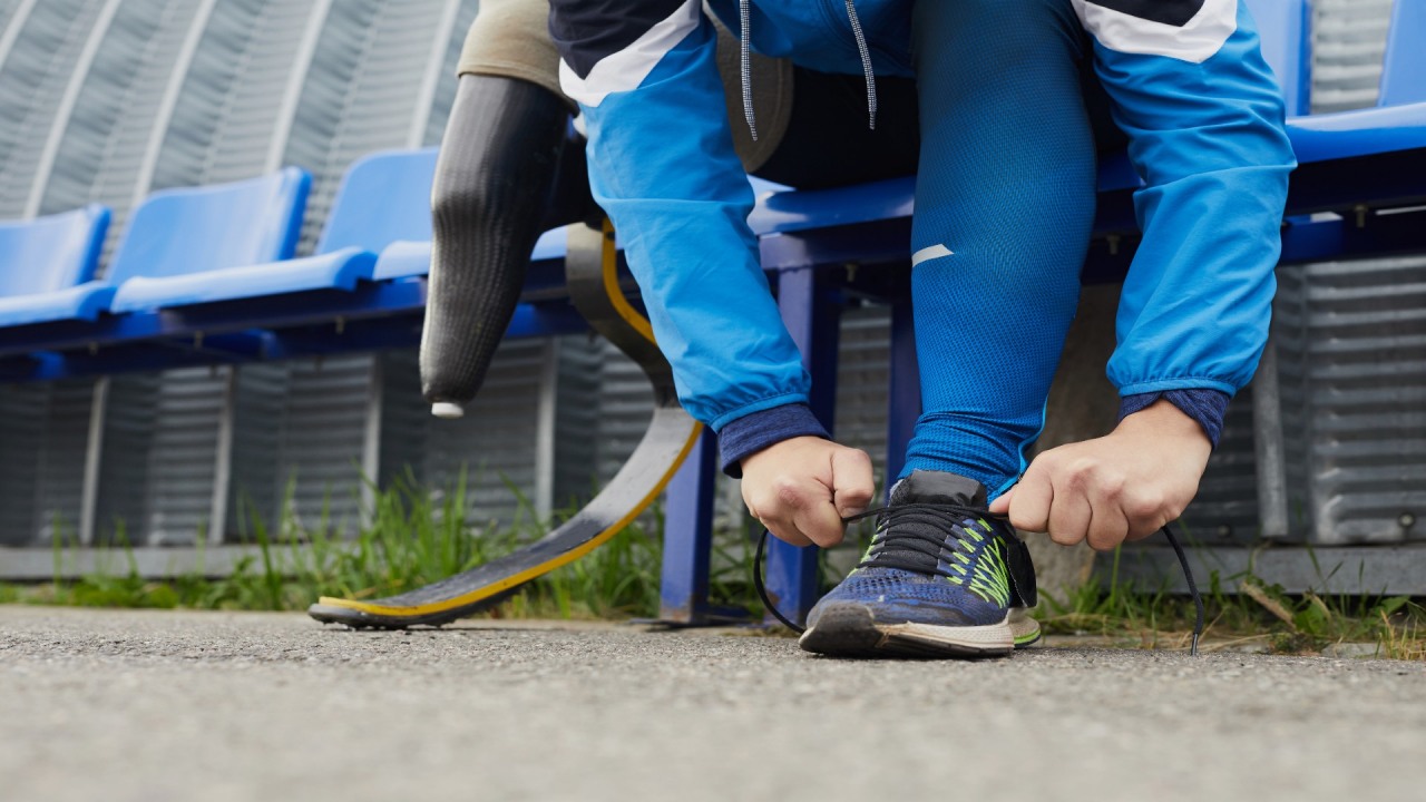 Fundacja ORLEN. Osoba z protezą nogi wiąże but i przygotowuje się do biegu na bieżni.